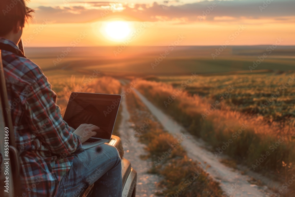 man engaged in remote work on his laptop amidst the countryside during a picturesque sunset, symbolizing modern agricultural practices. man engaged in remote work on his laptop amidst the countryside during a picturesque sunset, symbolizing modern agricultural practices.