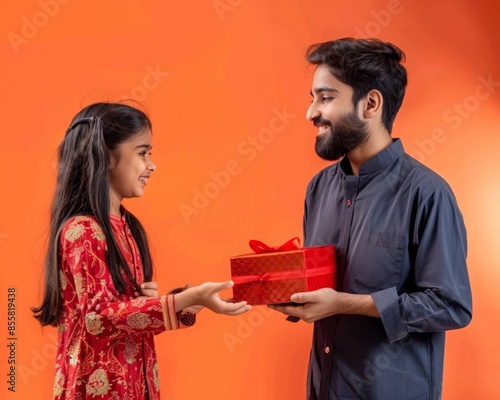 Cheerful Indian brother and sister exchanging gift box during Paksha Bandhan festival, yellow background. 
 Raksha Bandhan holiday concept, photo