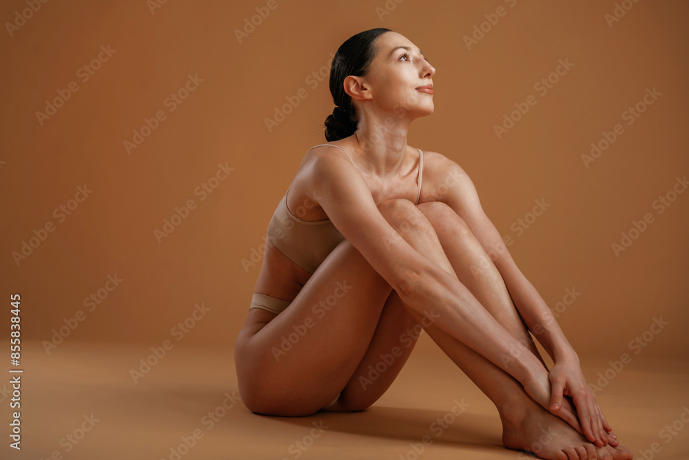 Sitting and resting on the floor. Woman with slim body shape is posing against background Sitting and resting on the floor. Woman with slim body shape is posing against background