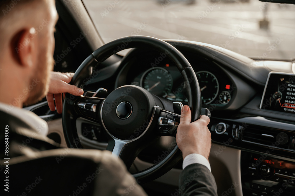 Close up view of steering wheel. Man in black suit is sitting in the car, driving Close up view of steering wheel. Man in black suit is sitting in the car, driving