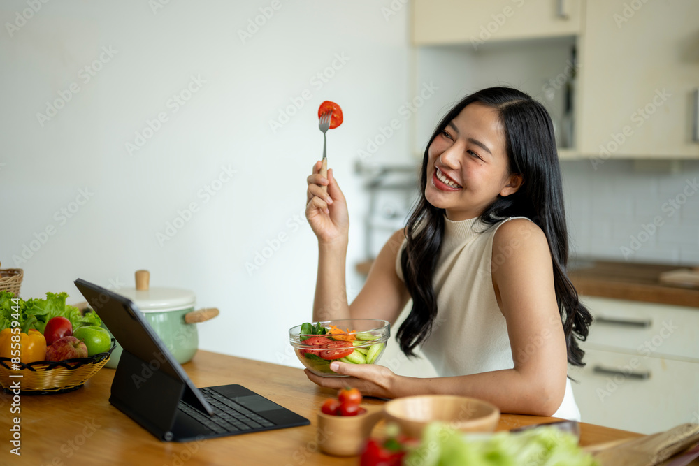 A woman is sitting at a table with a laptop and a bowl of salad