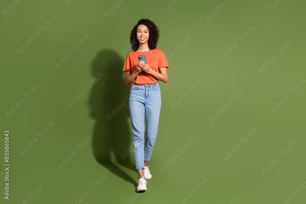 Full body photo of attractive young woman walk hold gadget dressed stylish orange clothes isolated on khaki color background Full body photo of attractive young woman walk hold gadget dressed stylish orange clothes isolated on khaki color background