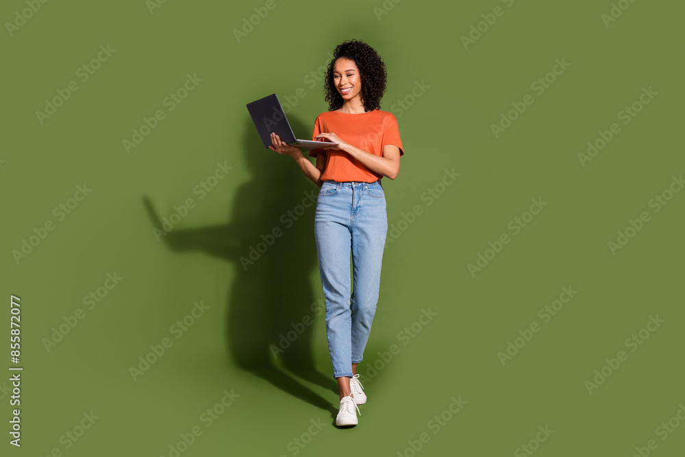 Full length photo of lovely young lady walk hold netbook dressed stylish orange garment isolated on khaki color background Full length photo of lovely young lady walk hold netbook dressed stylish orange garment isolated on khaki color background