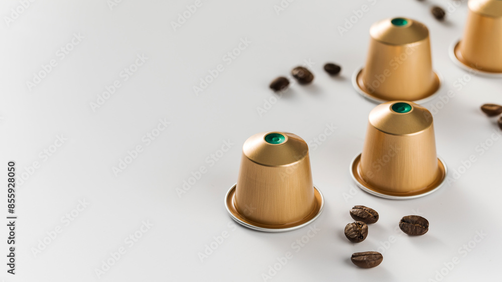 Golden coffee capsules and scattered beans on a white background. Copy space Golden coffee capsules and scattered beans on a white background. Copy space
