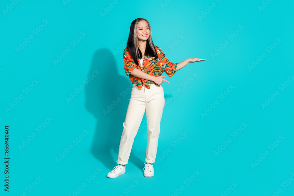 Full length photo of shiny attractive lady dressed print shirt pointing finger showing arm empty space isolated blue color background Full length photo of shiny attractive lady dressed print shirt pointing finger showing arm empty space isolated blue color background