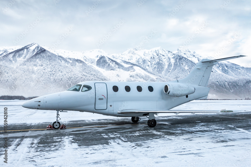 Naklejka premium White corporate airplane at winter airport apron on the background of high scenic snow capped mountains
