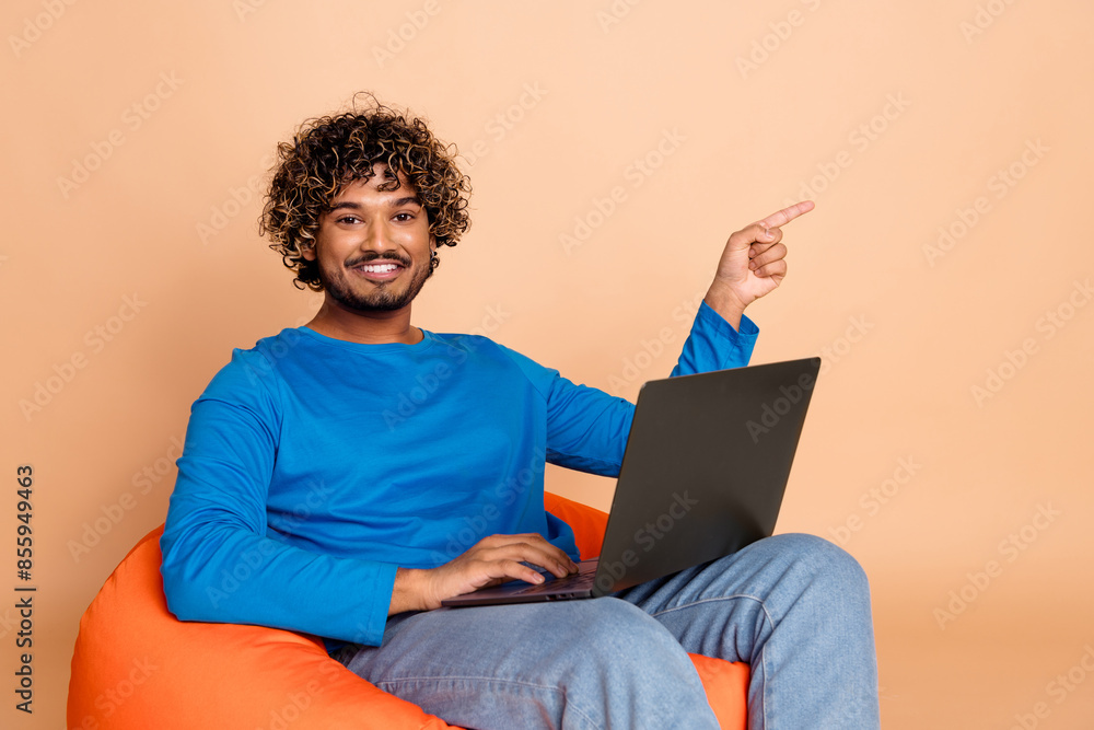 Photo of cheerful guy wear trendy clothes sit pouf recommend empty space buy gadget isolated on beige color background Photo of cheerful guy wear trendy clothes sit pouf recommend empty space buy gadget isolated on beige color background