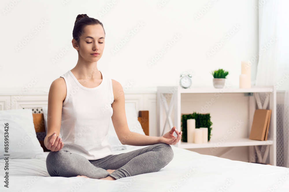 Woman meditating and practising yoga in the morning, sitting on bed, copy space Woman meditating and practising yoga in the morning, sitting on bed, copy space