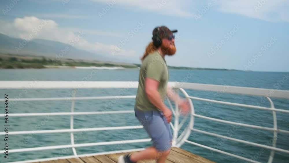 Crazy dancing on a wooden pier performed by a brutal man with a red beard spinning to music in headphones against the backdrop of the sea horizon. Crazy dancing on a wooden pier performed by a brutal man with a red beard spinning to music in headphones against the backdrop of the sea horizon.