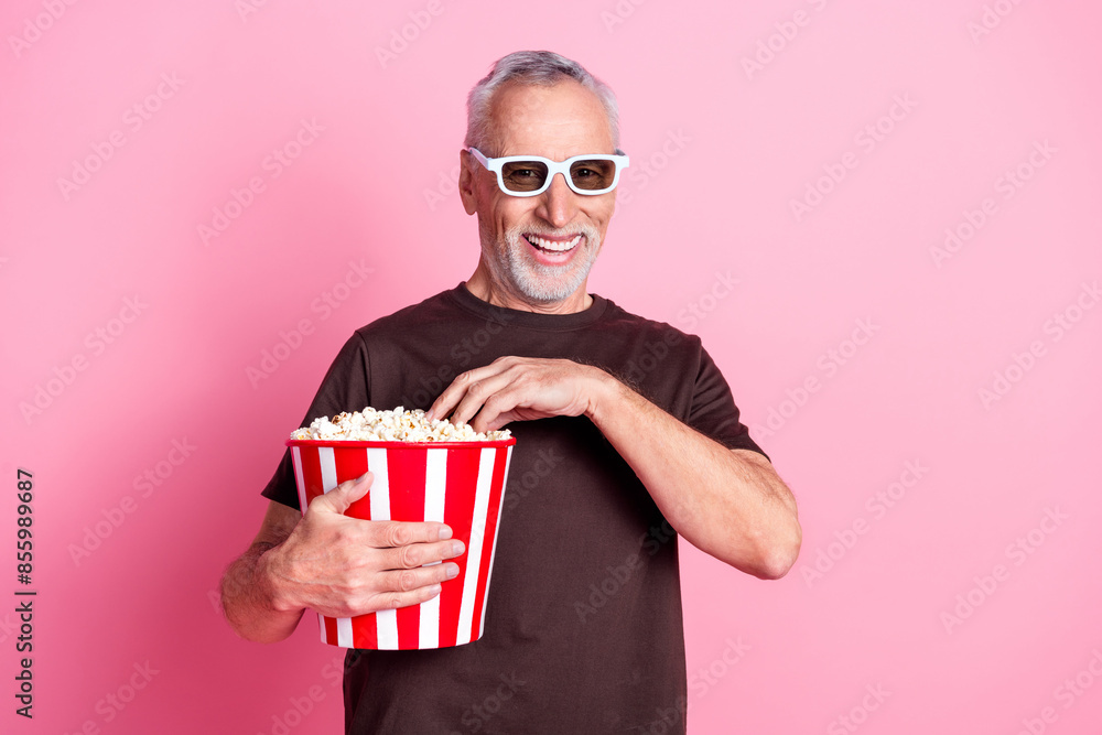 Portrait of funny positive man with beard dressed t-shirt in 3d glasses eat pop corn at movie premiere isolated on pink color background Portrait of funny positive man with beard dressed t-shirt in 3d glasses eat pop corn at movie premiere isolated on pink color background