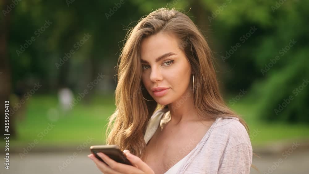 Young woman using smartphone outdoors in a summer park, looking focused and engaged with her device Young woman using smartphone outdoors in a summer park, looking focused and engaged with her device