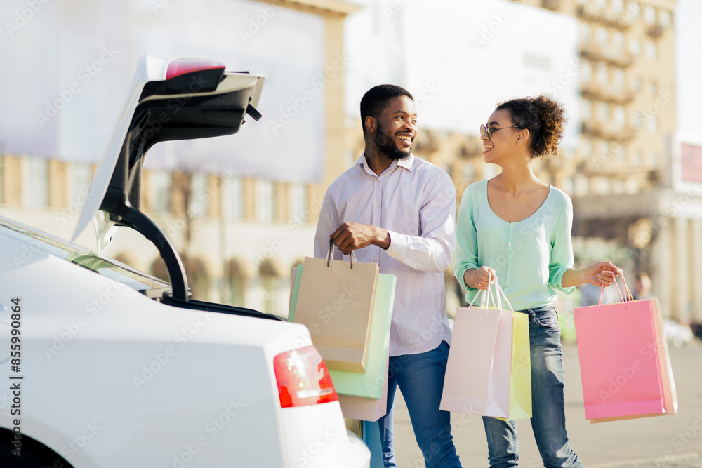 Φωτογραφία African American happy couple, dressed casually in jeans and shirts, are walking towards their car with a large number of shopping bags in their hands