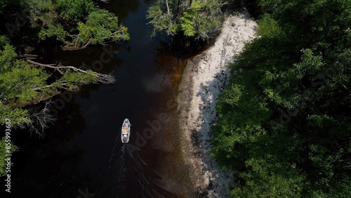 Fisherman on boat traveling on beautiful Black River past green forest and sandy river bank in South Carolina Low Country near Kingstree, SC photo