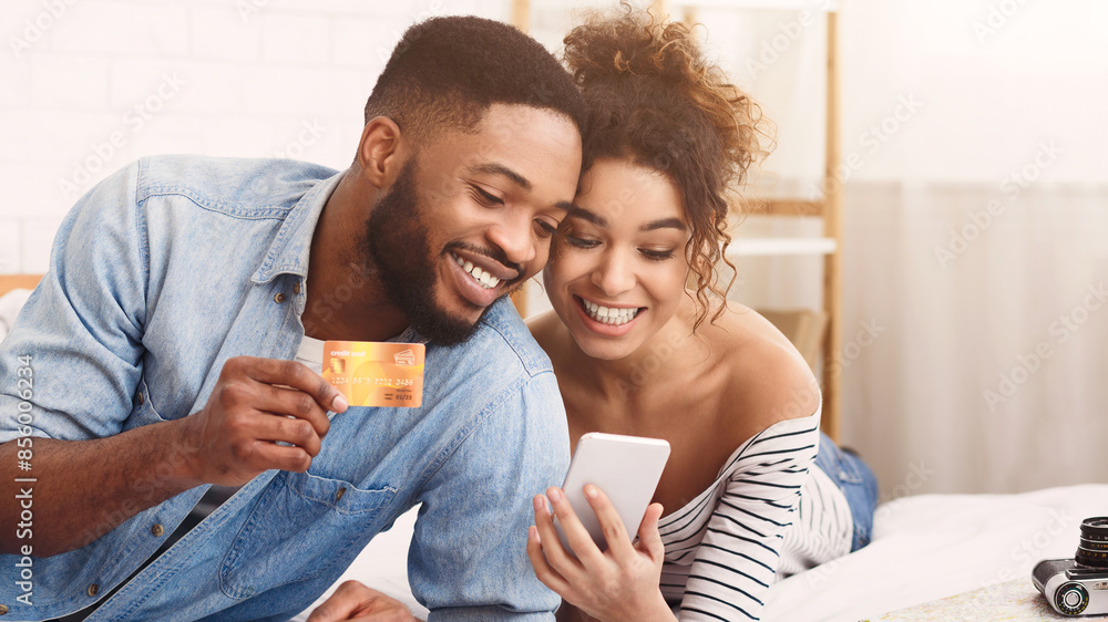 African American cheerful young couple sits closely together as they make an online purchase using a mobile phone and credit card. African American cheerful young couple sits closely together as they make an online purchase using a mobile phone and credit card.