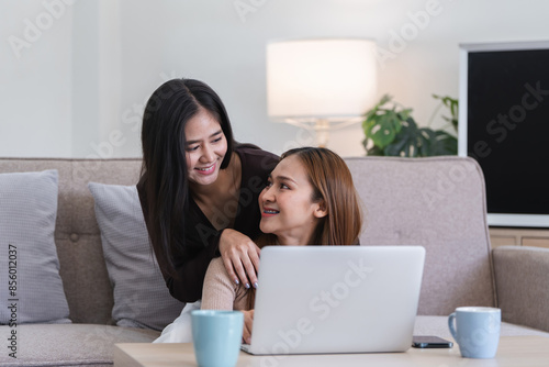 Happy LGBT Lesbian Couple Sitting Together on Couch with Laptop in Cozy Living Room photo