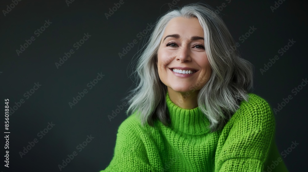 A portrait of a joyful mature woman with a beaming smile wearing a vibrant green sweater against a dark background A portrait of a joyful mature woman with a beaming smile wearing a vibrant green sweater against a dark background