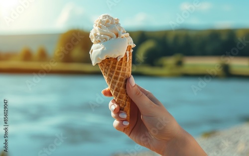 Obraz na płótnie Woman's hand holding a melting ice cream in a waffle cone against a summer landscape by the river w salonie