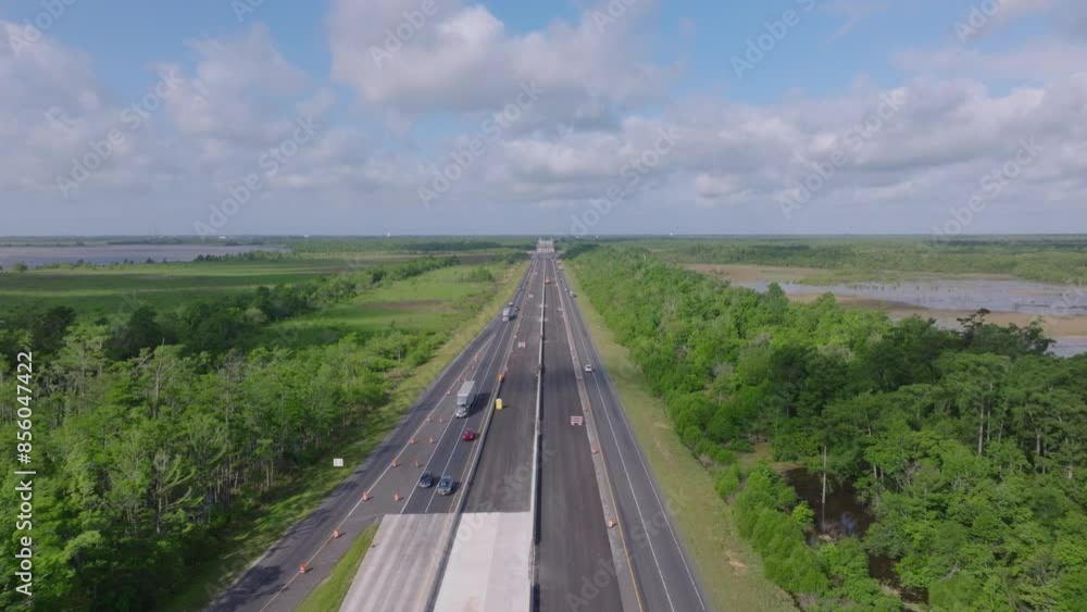 Aerial view of cars on a highway cutting through lush wetlands and greenery in the USA. Blue sky with white clouds adds to the scenic view Aerial view of cars on a highway cutting through lush wetlands and greenery in the USA. Blue sky with white clouds adds to the scenic view