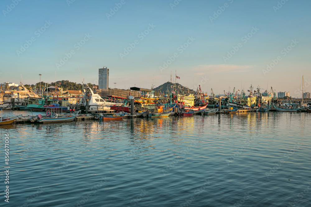 A panoramic view of a harbor filled with docked fishing boats, with the setting sun casting a warm glow on the water and boats. A panoramic view of a harbor filled with docked fishing boats, with the setting sun casting a warm glow on the water and boats.