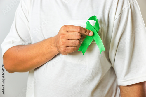 A person wearing a white shirt points to a green awareness ribbon on their chest, symbolizing support for a cause such as organ donation or mental health.