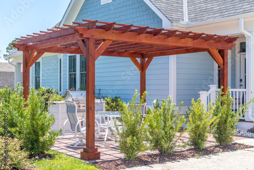 Obraz na płótnie Trendy outdoor patio pergola shade structure made of dark wood, awning and patio roof, white dining table, white chairs, metal grill surrounded by landscaping in a luxury American neighborhood w salonie