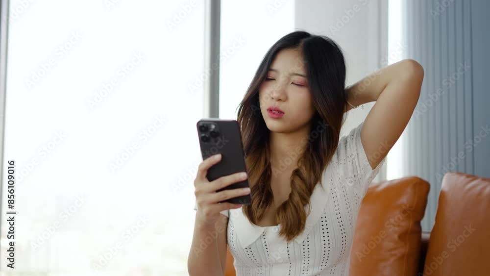 Stressed young asian woman suffering from neck pain while texting on her smartphone at home, female try to relax and dissolve ache by hand while suffers from tension discomfort indoors Stressed young asian woman suffering from neck pain while texting on her smartphone at home, female try to relax and dissolve ache by hand while suffers from tension discomfort indoors