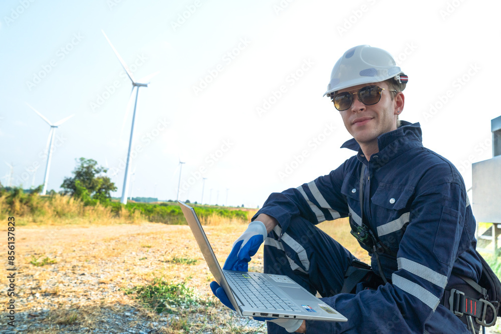 A technician in safety gear meticulously records data with a wind turbine in the backdrop at dusk. A technician in safety gear meticulously records data with a wind turbine in the backdrop at dusk.