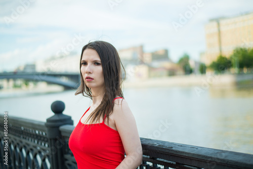 A woman in a red dress stands on a bridge overlooking a pond. She looks into the distance, perhaps lost in thought. Loneliness and contemplation concept