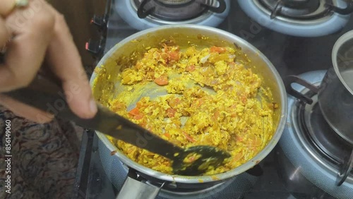 A woman's hand making tasty egg burji masala in a steel pan, while stirring and scrambling the food ingredients in the kitchen for dinner photo