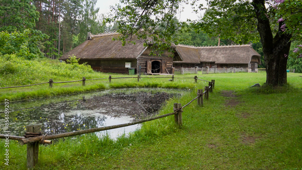 This is an old wooden barn located in the forests of Riga Latvia in a park that preserves an ancient village from medieval times. Nearby there is a water well This is an old wooden barn located in the forests of Riga Latvia in a park that preserves an ancient village from medieval times. Nearby there is a water well