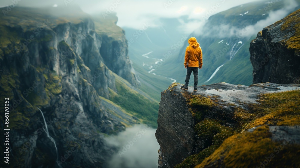 Obraz premium A man in a yellow jacket stands on top of a mountain, against a mountain landscape.
