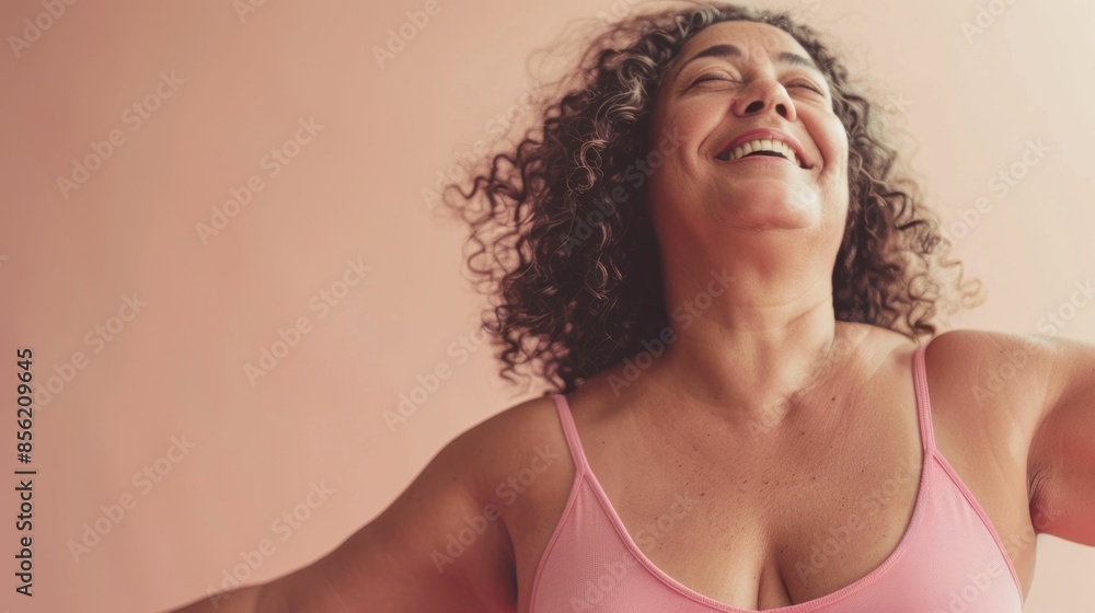 A joyful woman with curly hair wearing a pink top laughing and raising her arms in a moment of happiness. A joyful woman with curly hair wearing a pink top laughing and raising her arms in a moment of happiness.