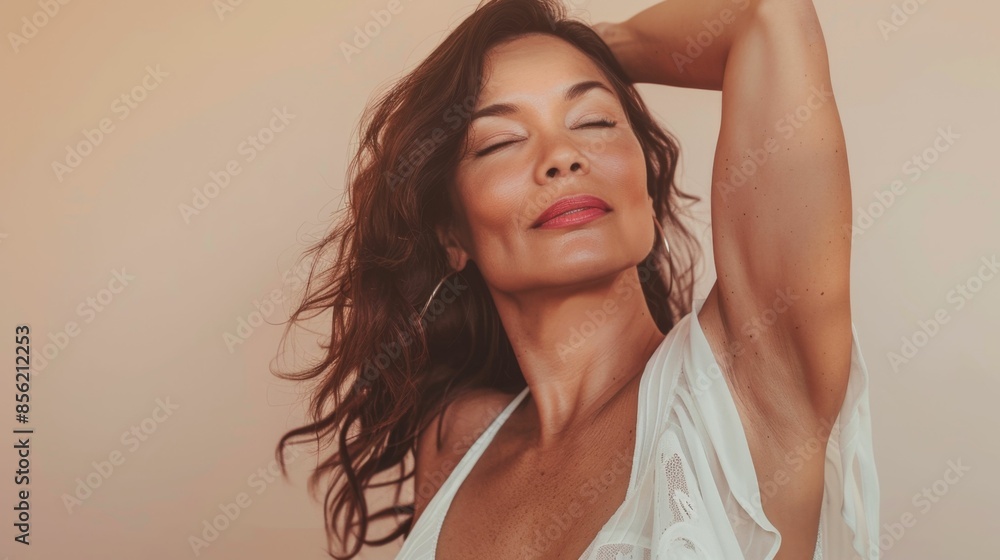 A woman with closed eyes wearing a white top with her arm raised against a soft-focus beige background. A woman with closed eyes wearing a white top with her arm raised against a soft-focus beige background.