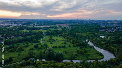 Aerial view of a suburban area with industrial buildings and city skyline in the background under a soft evening sky with gentle clouds.