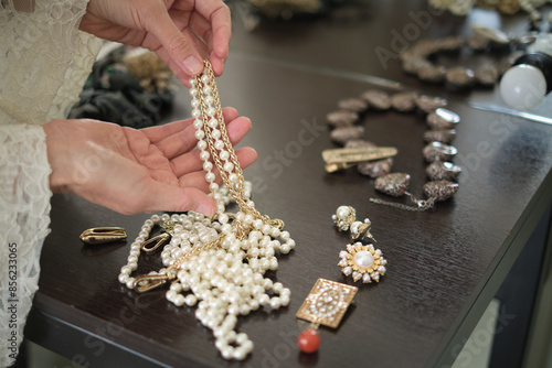 A person holds a pearl necklace over a table filled with various pieces of jewelry. This image showcases the elegance and beauty of fine accessories. photo