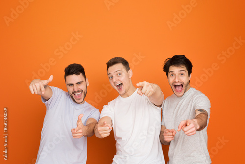 Obraz na plátně A trio of european friends joyfully point at the camera, an invitation to join t