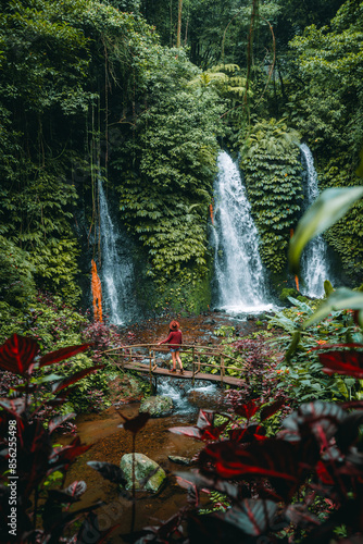 This set of Twin Waterfalls is one of the five waterfalls found in the Banyu Wana Amertha Waterfall area. A woman is standing on the bridge, wondering at the beauty of the waterfall. photo