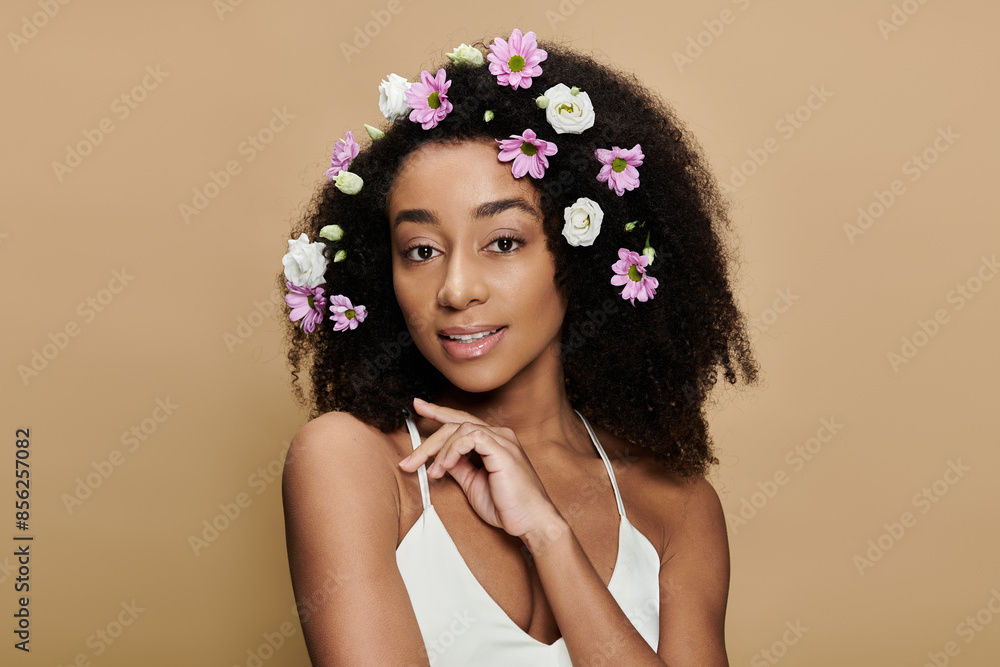 Naklejka premium A beautiful African American woman with natural makeup and flowers in her hair smiles softly for the camera against a beige background.