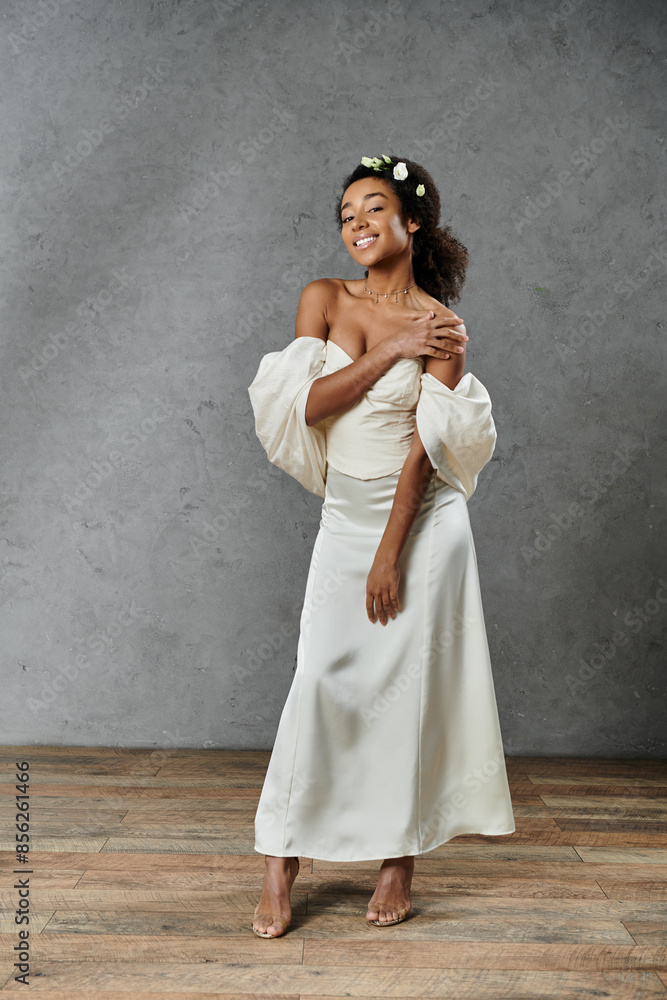 An African American bride in white dress, flowers in hair, beaming with joy against grey backdrop. An African American bride in white dress, flowers in hair, beaming with joy against grey backdrop.