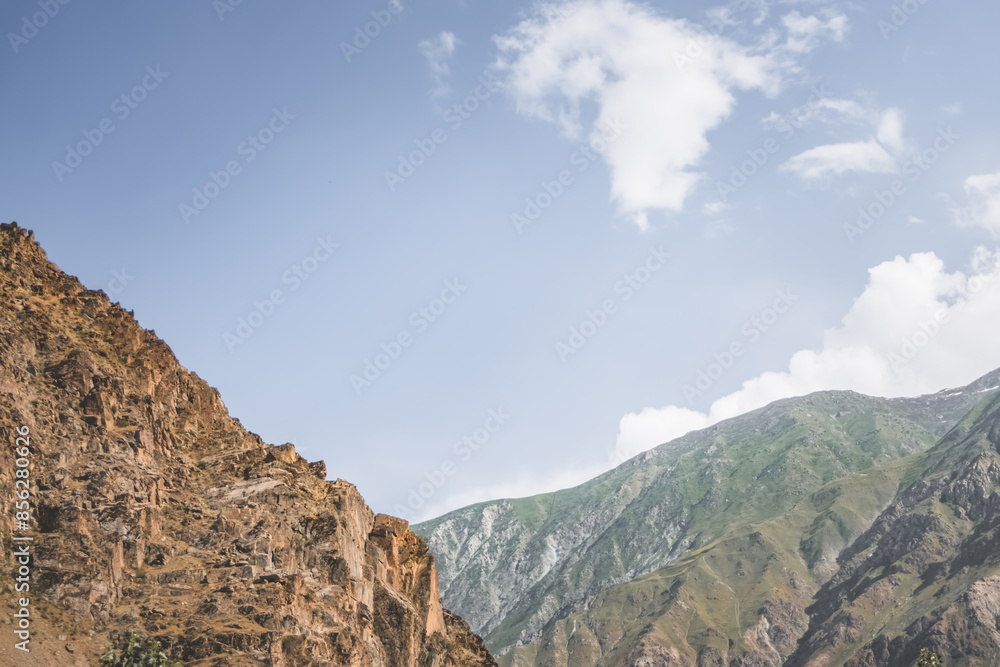Minimalistic mountain peaks and slopes of rocks with vegetation against the blue summer sky on a sunny summer day in the mountains of Tajikistan in the Pamirs