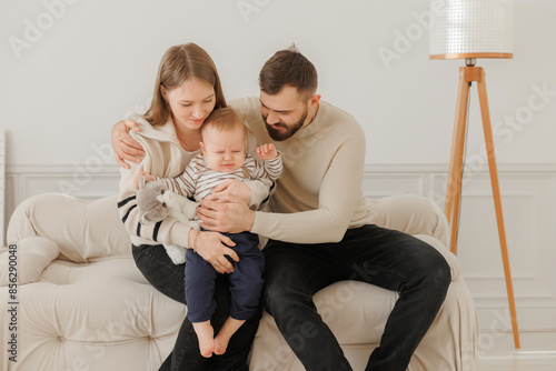 Photos Gentle moment, young mom woman and dad man comfort their fussy toddler on sofa, surrounded by tranquility of their home