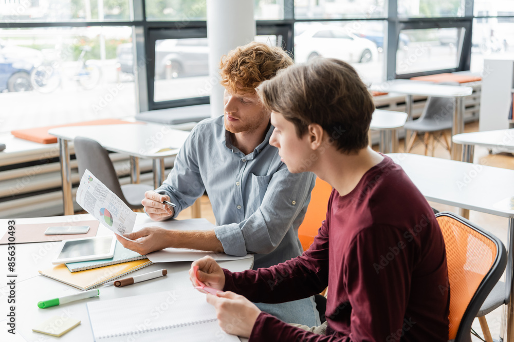 Two male students deeply focused on their studies at a table. Two male students deeply focused on their studies at a table.