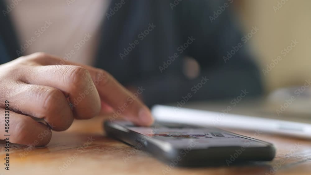 A person is pointing at a cell phone on a table. The phone is black and has a cracked screen. The person is wearing a blue shirt A person is pointing at a cell phone on a table. The phone is black and has a cracked screen. The person is wearing a blue shirt