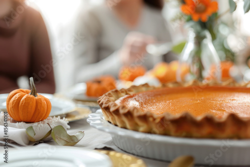 Thanksgiving family dinner. Traditional pumpkin pie and vegan meal close up, with blurred happy people around the table celebrating the holiday.