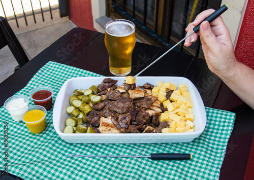 Tray with minced cucumber, cheese, chicken meat and beef in a table. Appetizer called 'picadinho' in Brazil. Glass of beer and sauces on the side. photo