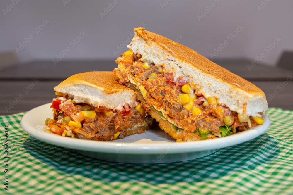 Delicious fresh beef strogonoff burger cut in half, with bread, beef, cheese, tomatoes, lettuce, egg, corns, peas and sauce. This type os food is known as xis in Brazil. Delicious fresh beef strogonoff burger cut in half, with bread, beef, cheese, tomatoes, lettuce, egg, corns, peas and sauce. This type os food is known as xis in Brazil.
