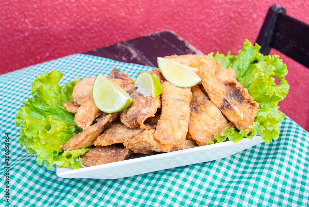 Portion of crunchy breaded deep fried fish in cubes, with lettuce below and lemon on top, on a table, in close-up. Portion of crunchy breaded deep fried fish in cubes, with lettuce below and lemon on top, on a table, in close-up.