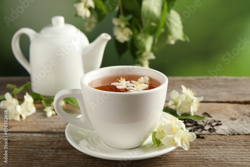 Aromatic jasmine tea in cup, flowers, dry leaves and teapot on wooden table outdoors