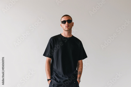 Stylish Young Man Wearing Black T-Shirt and Sunglasses Posing Against White Background photo