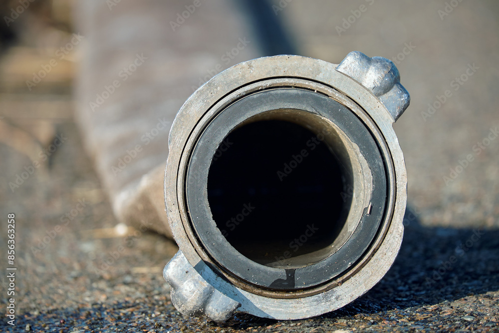 Close-up of a metal hose fitting lying on a rough surface, showcasing the texture and industrial design of the component. Ideal for themes related to industry, engineering, and machinery. Close-up of a metal hose fitting lying on a rough surface, showcasing the texture and industrial design of the component. Ideal for themes related to industry, engineering, and machinery.